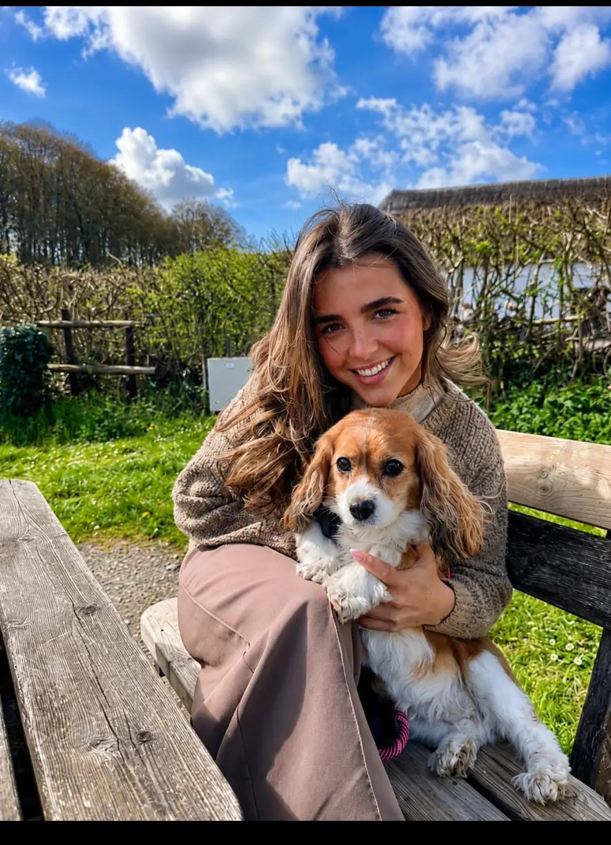 Maddie sitting on a garden bench in the sunshine, cuddling a Cavalier King Charles Spaniel